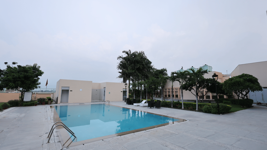 A serene outdoor swimming pool at Ramada by Wyndham Bodh Gaya Mahabodhi with a spacious deck, lush greenery and calm surroundings, perfect for relaxed leisure.