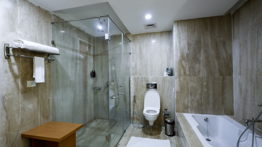 A modern bathroom featuring a large bathtub, shower, and stone-effect wall tiles at Ramada by Wyndham Bodh Gaya Mahabodhi.