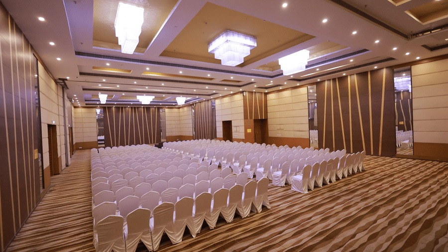 A large, elegant ballroom is set up in theatre-style with rows of white covered chairs at Ramada by Wyndham Bodh Gaya Mahabodhi.