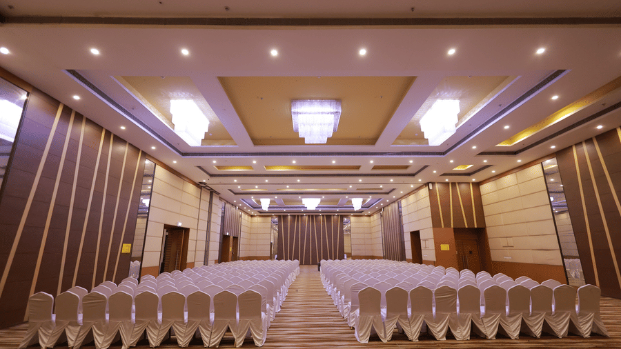 A ballroom with a large stage and the elaborate ceiling lighting at Ramada by Wyndham Bodh Gaya Mahabodhi.