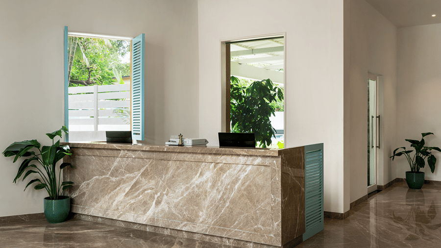 Reception desk in a bright lobby with windows and indoor plants.