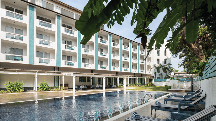 Large swimming pool surrounded by loungers and the hotel building.