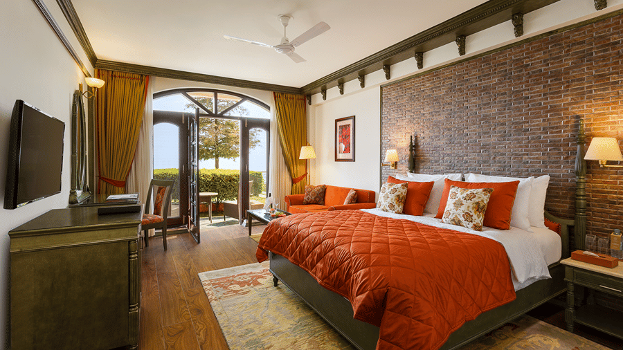 A bedroom with a queen size bed with an orange runner, a television, and glass doors leading outside at Ramada by Wyndham Mussoorie Mall Road.