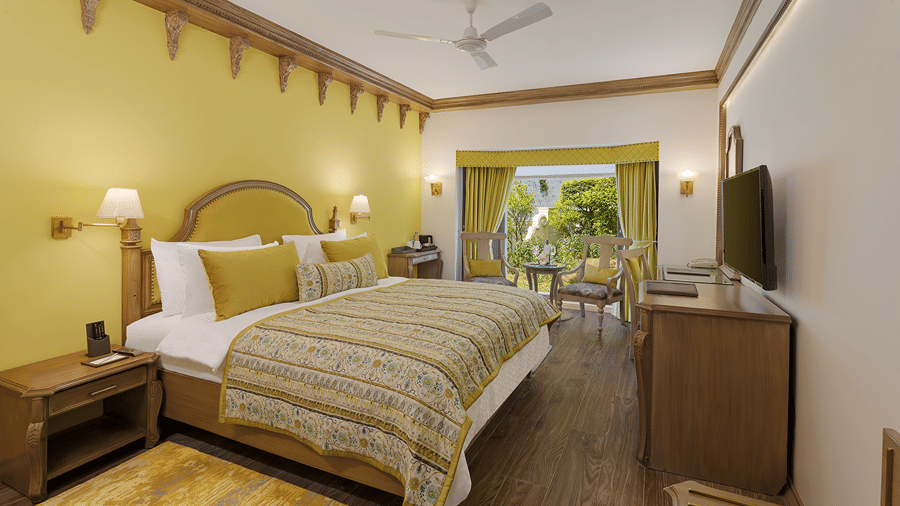 A room with a queen size bed with light linens, yellow accent walls, nightstands, wall-mounted television, and a desk area at Ramada by Wyndham Mussoorie Mall Road.