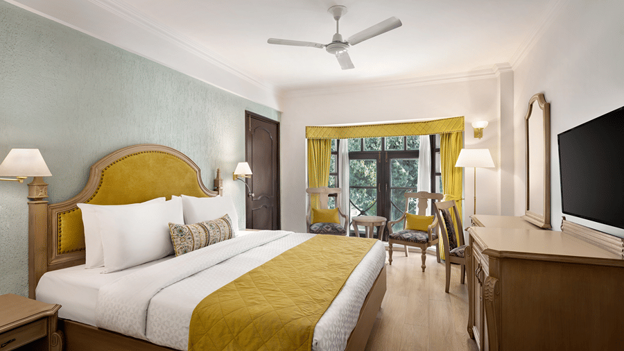 A room featuring a queen size bed with yellow accents, a ceiling fan, and a desk area at Ramada by Wyndham Mussoorie Mall Road