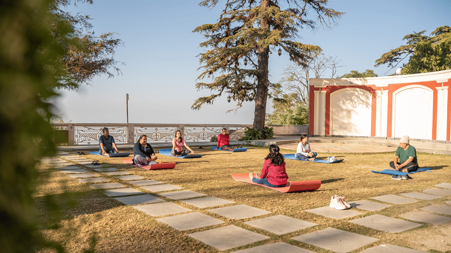 People sitting on yoga mats on an outdoor paved terrace surrounded by trees at Ramada by Wyndham Mussoorie Mall Road.