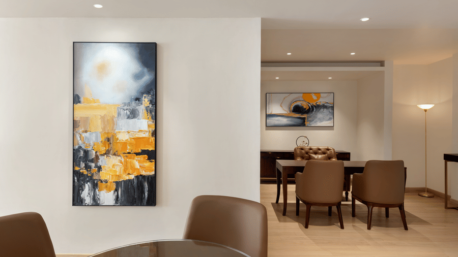 Modern suite interior with a bold yellow abstract painting, a dining table with chairs, and an open-plan layout with warm neutral tones.