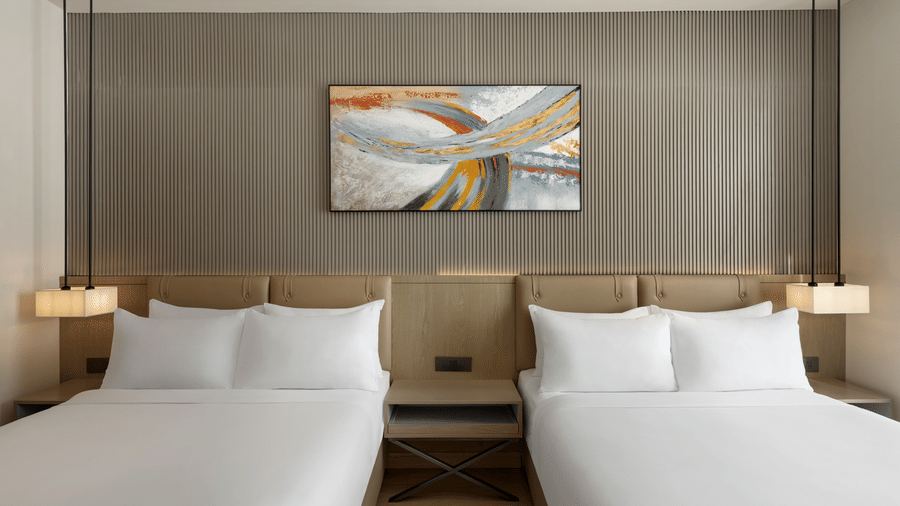 Elegantly designed king size bedroom at Ramada by Wyndham Sonipat Murthal, with crisp white linens, a padded headboard, pendant bedside lights, and a bold abstract wall painting.