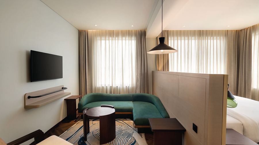 Ramada Encore by Wyndham, Bhiwadi | Hotel room with green couch, bed, TV, and decorative lighting.