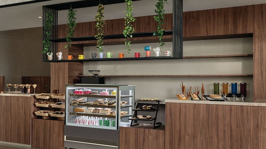 Ramada Encore by Wyndham, Bhiwadi | Cafe counter with pastries, drinks, and a display case. Wooden cabinets.