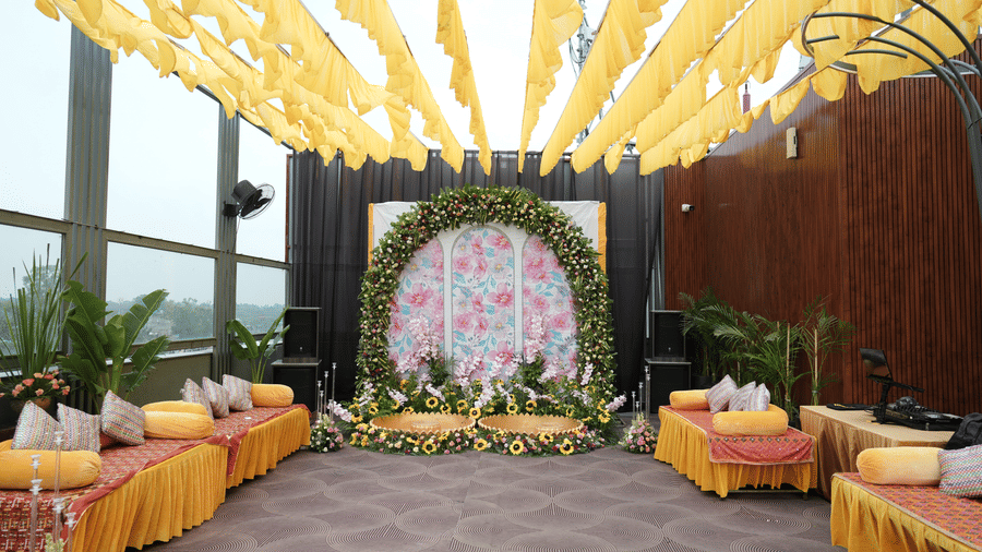 Rooftop event setup at Ramada Encore by Wyndham Chandigarh Zirakpur, featuring yellow drapes overhead, floral stage backdrop, cushioned seating, and vibrant decor ideal for weddings and celebrations.