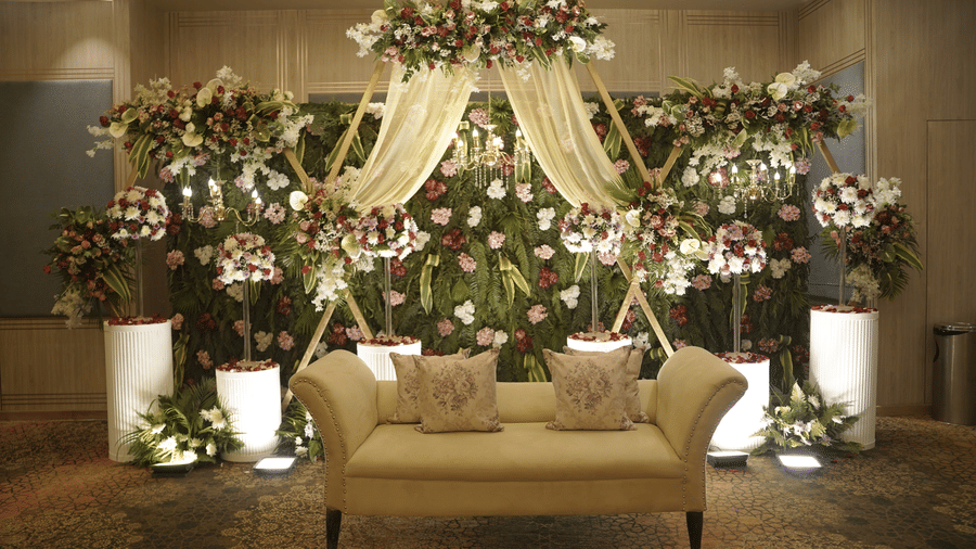 Indoor floral stage at Ramada Encore by Wyndham Chandigarh Zirakpur, featuring a lush flower wall, elegant drapes, soft lighting, and a classic sofa.