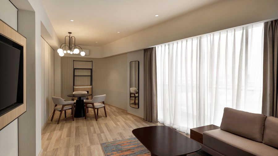 Spacious hotel suite living area at Ramada Encore by Wyndham Gurugram Dwarka Expressway, featuring comfortable seating, a television and natural light.