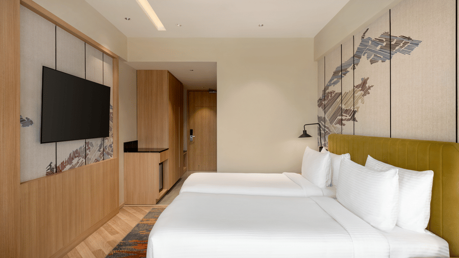 Well-appointed hotel room at Ramada Encore by Wyndham Gurugram Dwarka Expressway, featuring twin beds, a television and contemporary wooden furnishings.