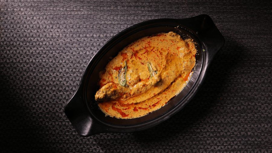 A rich, creamy yellow curry dish served in an elegant oval black bowl.