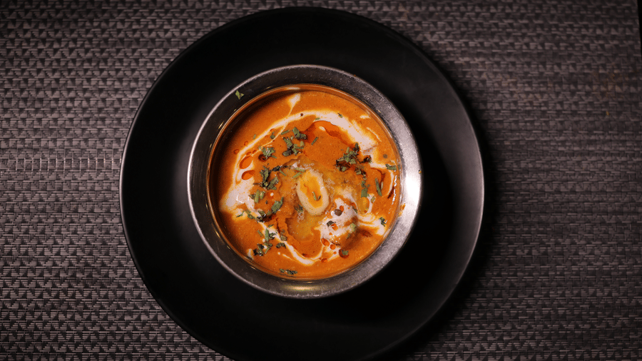 A bowl of creamy orange curry garnished with herbs and cream, served on a black plate.