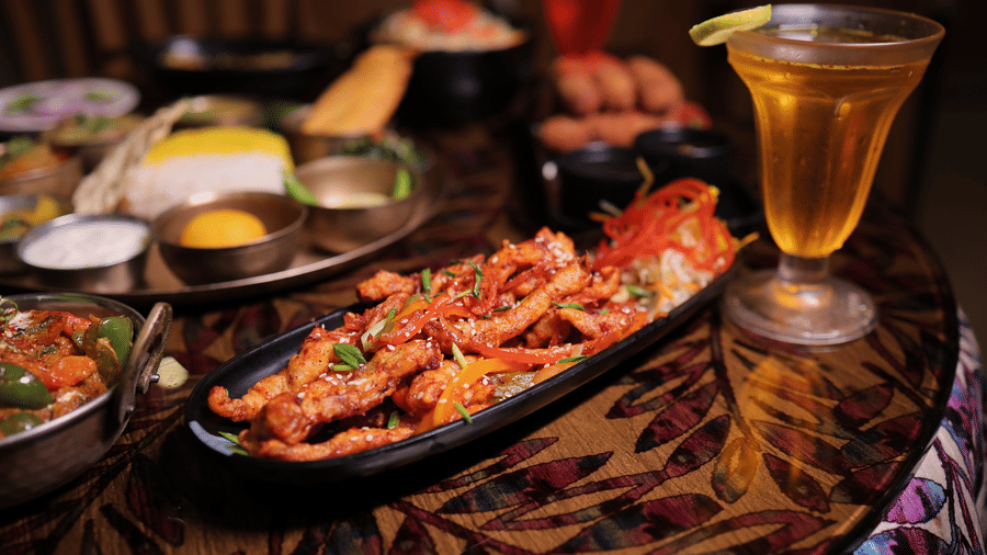 A delicious Indian food spread on a dining table, accompanied by a tall glass of cold yellow beverage.