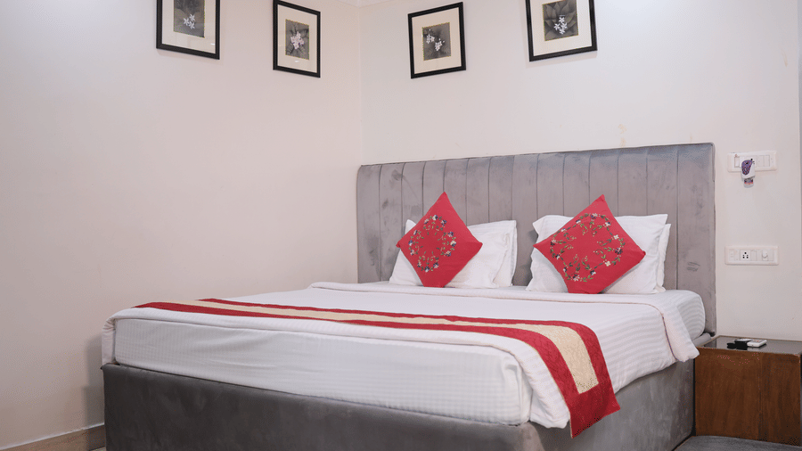 A spacious double bed with crisp white linen and decorative red cushions under four small picture frames on the wall.