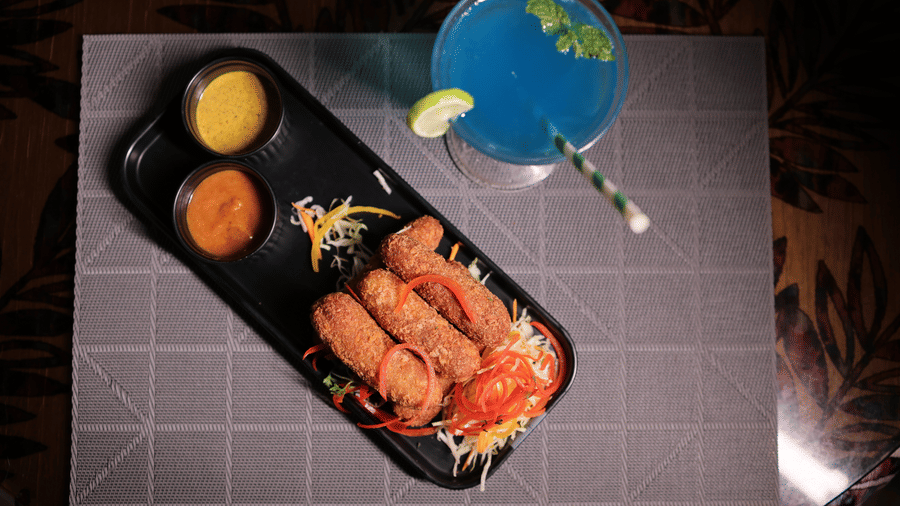 A platter of crispy fried starters served with dips alongside a refreshing blue cocktail garnished with mint.