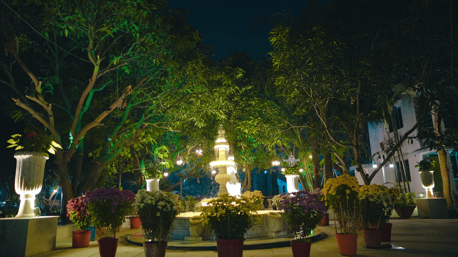 A beautiful stone fountain lit up at night, surrounded by potted plants and trees in a resort courtyard.