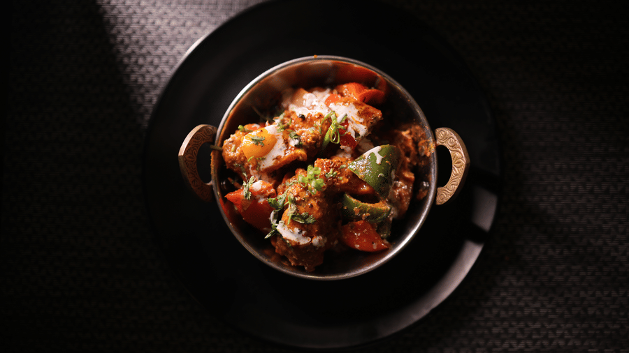 A savoury Indian curry dish served in a traditional metal bowl on a dark textured table.