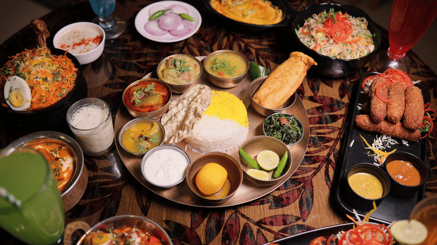 An elaborate spread of Indian cuisine featuring a central thali platter, curries, rice, and colourful drinks.