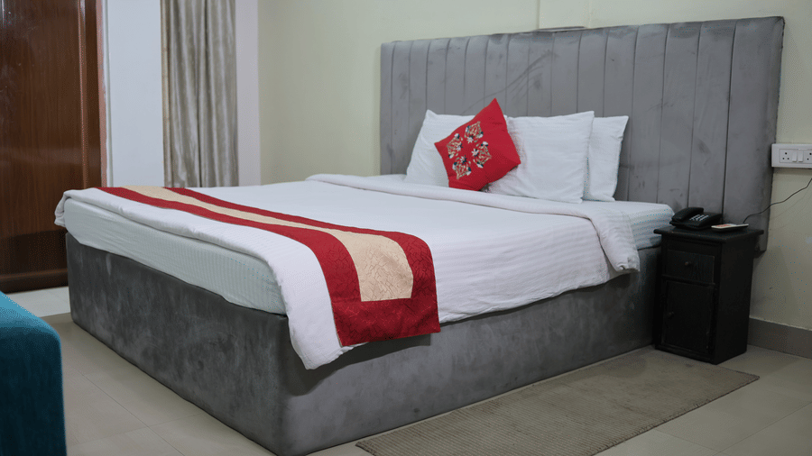 A double bed with a tall grey upholstered headboard, white bedding, and a single red accent cushion.