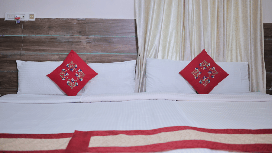 A close-up view of a neatly made hotel bed with white linen and vibrant red square accent pillows.