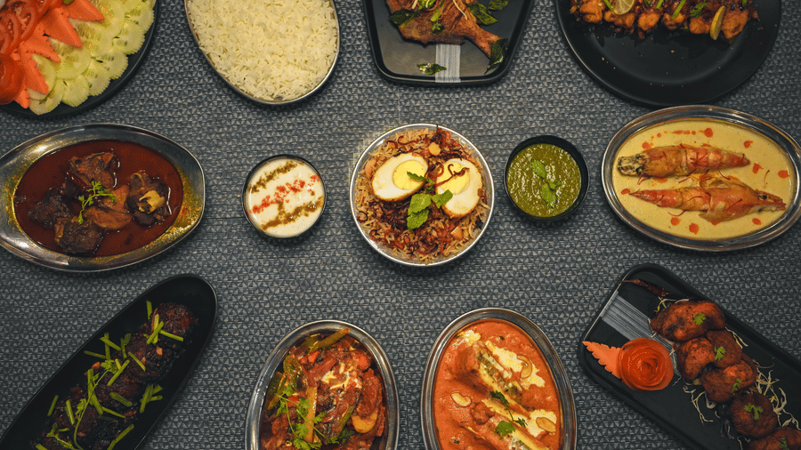 A top-down flat lay view of multiple Indian dishes including rice, curries, and side dishes arranged on a dark table.