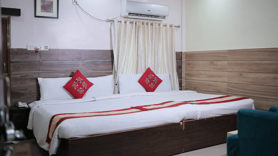 A cosy hotel bedroom featuring a large double bed dressed in clean white sheets with red decorative cushions.