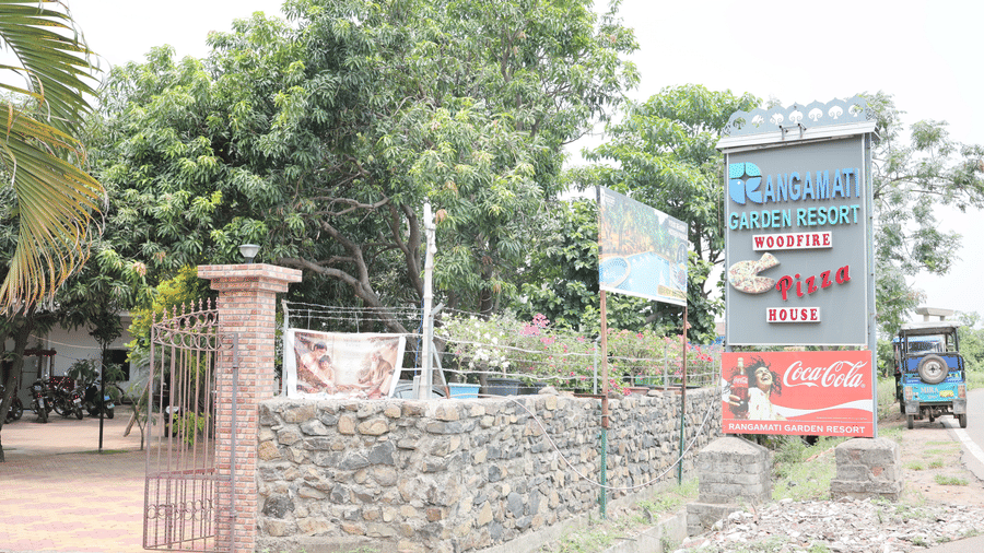 A stone wall and gated entrance to a resort, featuring a tall signpost on the right side.