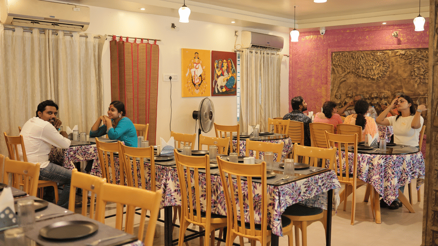 An indoor restaurant dining hall with several wooden tables, chairs, patterned table runners, and guests dining.