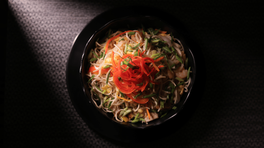 A top-down view of a savoury noodle dish garnished with colourful vegetables, served in a black bowl.