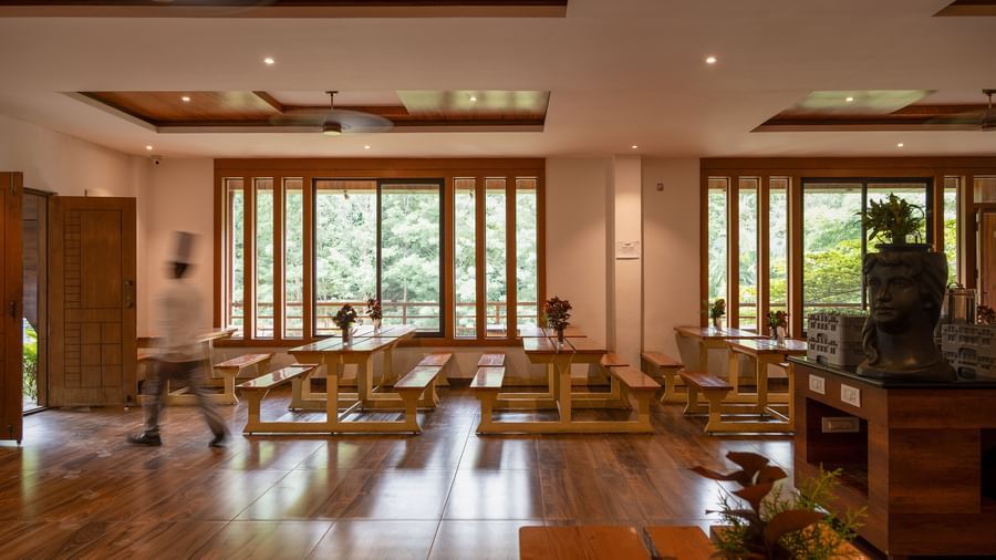 A spacious dining hall with wooden floors and high ceilings offers multiple tables and chairs, with large glass doors opening to an outdoor area | Lake View Restaurant