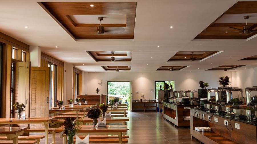 A well-lit restaurant interior features a buffet line on the left and dining tables with chairs on the right, all under a decorative wooden ceiling | Lake View Restaurant