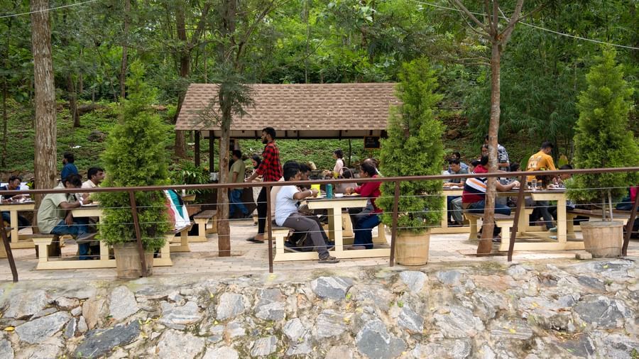 An outdoor seating area with tables and chairs is set under a wooden shelter in a natural, green environment | Lake View Restaurant