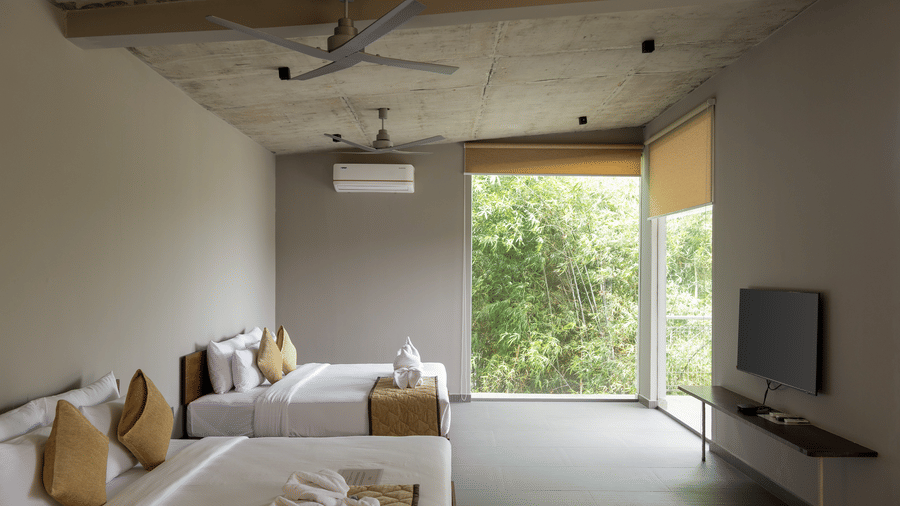 A bedroom with a large bed, a ceiling fan, a television, and a panoramic view of the outdoors through a large window | Gaia Studio | RD's Nature Retreat, Bangalore