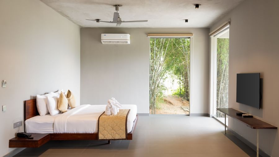 A minimalist bedroom with a large bed, a television, and an open doorway leading to an outdoor area | Gaia Studio | RD's Nature Retreat, Bangalore