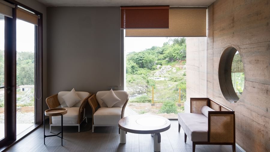 A room with a seating area near a large window, two armchairs, a small table, and a view of the natural landscape | Gaia Studio | RD's Nature Retreat, Bangalore