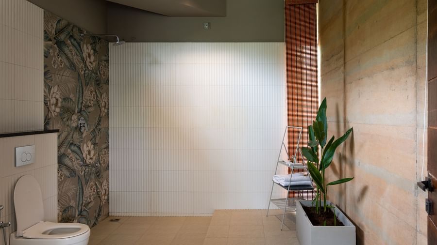 A bathroom with a toilet, a plant in a pot, and a large window or opening revealing an outdoor area | Gaia Studio | RD's Nature Retreat, Bangalore