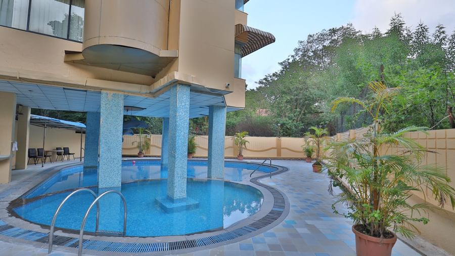 An outdoor swimming pool with blue water, surrounded by paved areas and the hotel building - Retreat Heritage, Lonavala