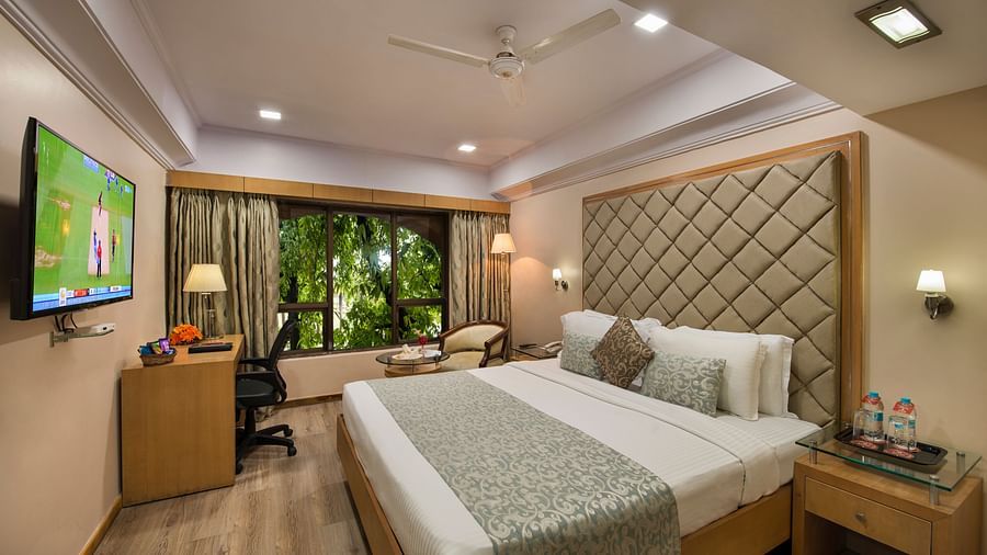 Hotel room with a neatly made bed, a TV on the wall, and a view of greenery - Lords Inn Vadodara