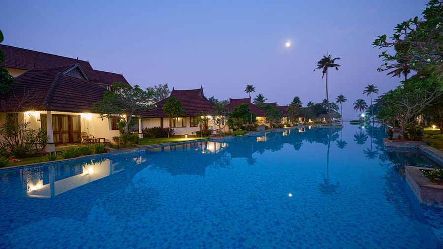 an image of night view of a swimming pool with rooms illuminating yellow lights - Rhythm Kumarakom