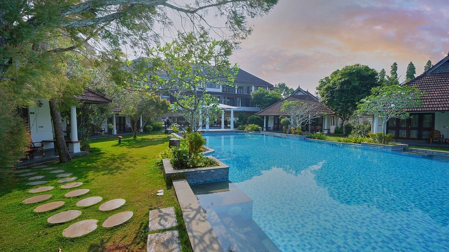 an image of a swimming pool surrounded by rooms and grasslands - Rhythm Kumarakom