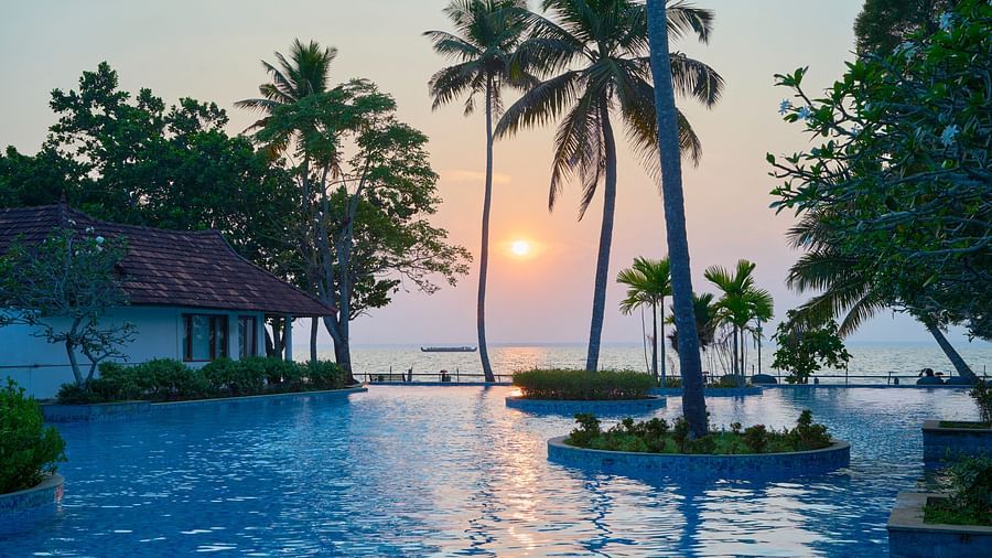 an image of a swimming pool with a sunset glowing in the background. - Rhythm Kumarakom