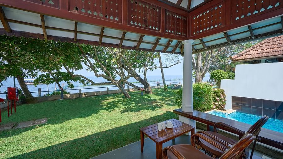 an image of a patio space featuring classic wooden architecture that provides a shady spot to sit and enjoy views of a beautiful garden and a calm swimming pool  - Rhythm Kumarakom