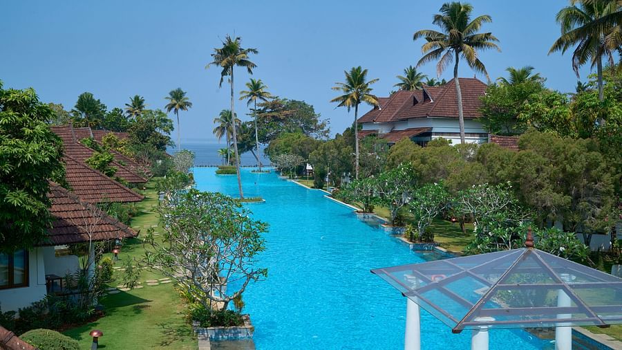 india's largest swimming pool with rooms on one side and trees on another - Rhythm Kumarakom