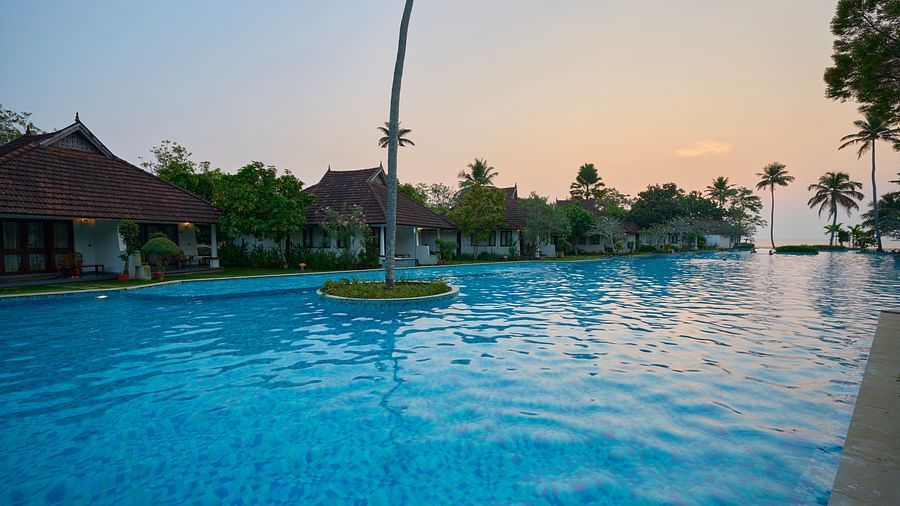 an image of a swimming pool with rooms and trees on each sides - Rhythm Kumarakom