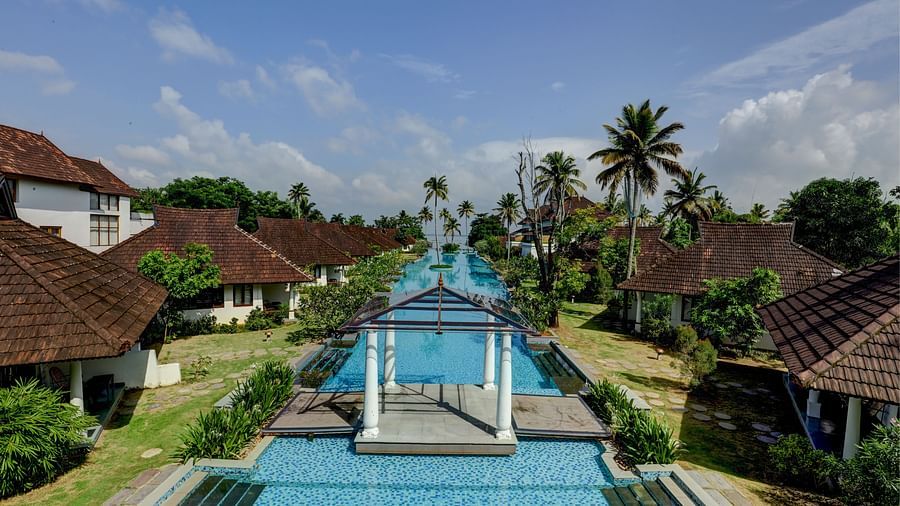 an image of a swimming pool with rooms surrounded  by garden - Rhythm Kumarakom