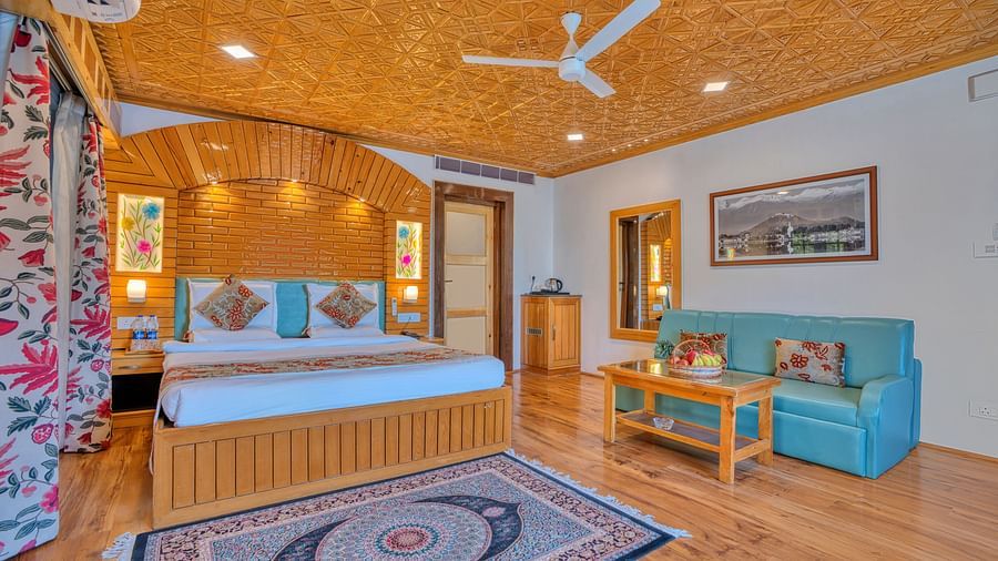 Cosy suite with wooden bed frame, teal sofa and warm lighting at Royal Comfort Regency, suited for both leisure and business stays.